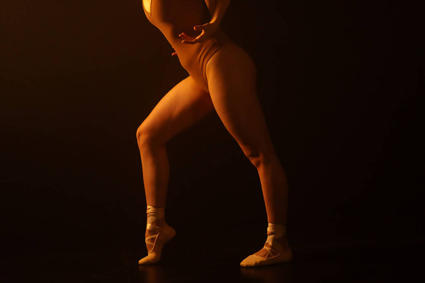 Young ballerinas fluidity and precision are on display as she performs on pointe. The play of light and shadows casts a dramatic ambiance, emphasizing the elegance of her smooth movements on a dark - Foto, Imagen