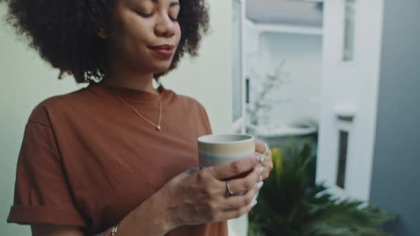 Tilt up πλάνο της νεαρής γυναίκας πίνοντας καφέ στέκεται στο μπαλκόνι στο σπίτι την Κυριακή το πρωί - Πλάνα, βίντεο