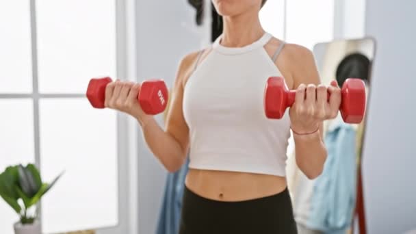 A focused young woman exercises with dumbbells in a bright, modern living room - Footage, Video
