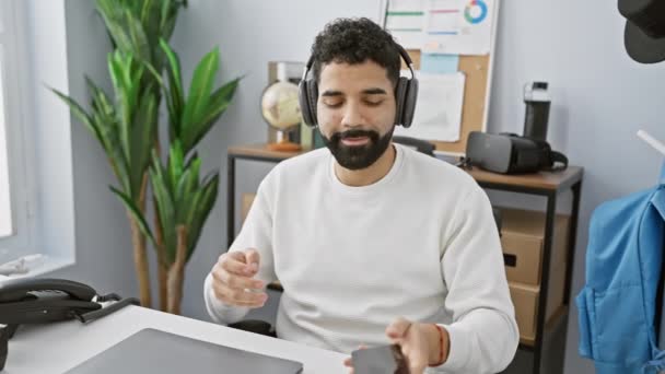 A cheerful young hispanic man with a beard enjoys dancing while working in a modern office setting, evoking a relaxed and joyful atmosphere. - Footage, Video