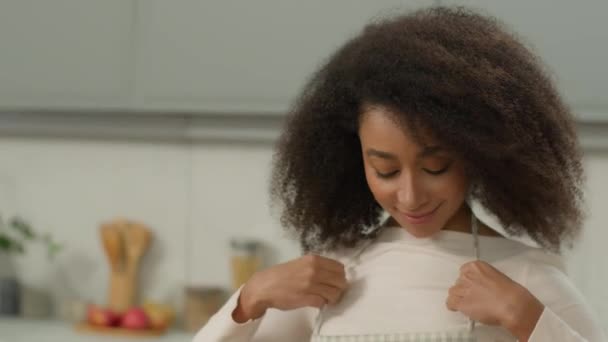 Šťastný zdravý úsměv Afroameričanka žena hospodyňka šéfkuchařka etnická dívka žena doma moderní kuchyně dát na zástěru domácnosti domácí práce připravit na vaření výživy dodávky potravin vařit domácí jídlo - Záběry, video