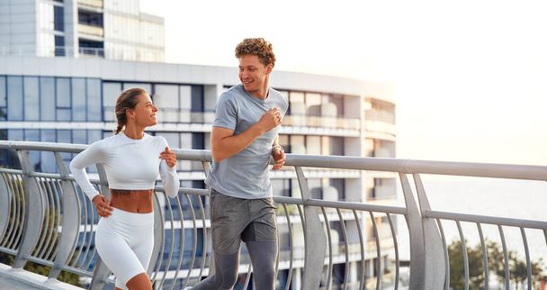 Una pareja en ropa deportiva corriendo al aire libre en un puente. Ejercicios matutinos y trotar. Deportes y recreación, estilo de vida activo. - Foto, imagen