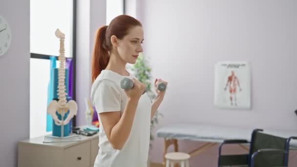 Een jonge vrouw oefeningen met halters in een revalidatie kliniek kamer, impliceert fysiotherapie en herstel. - Video
