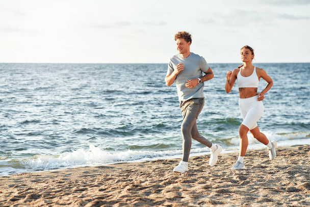 Ένα ζευγάρι με αθλητικά να τρέχει στην ακτή δίπλα στη θάλασσα. Πρωινές ασκήσεις και τρέξιμο. Αθλητισμός και αναψυχή, ενεργός τρόπος ζωής. - Φωτογραφία, εικόνα