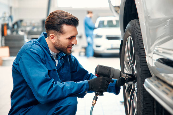 Car mechanic working in garage and changing wheel alloy tire. Repair or maintenance auto service. Mechanic holding a tire tire at the repair garage, replacement of winter and summer tires. - Photo, Image