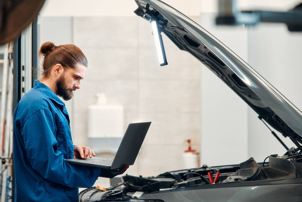 Mechanic in uniform repairing a car in a workshop. Auto mechanic detailed inspection of the car. Auto car repair service center. Car service, repair, maintenance concept. - Photo, Image