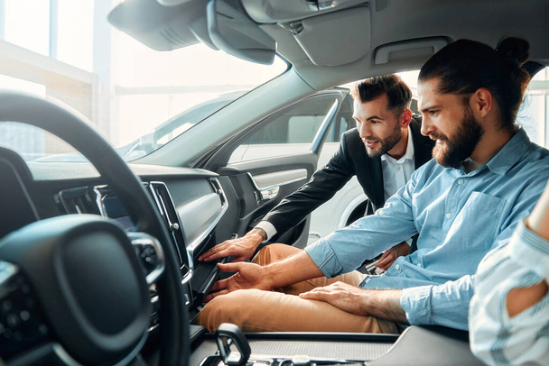 A couple is sitting in a car at a car dealership and receiving advice from a salesperson. Purchase, rental and insurance of a car. - Photo, Image
