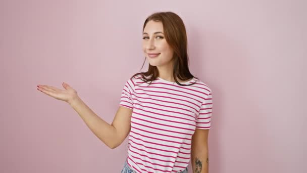 Jeune fille brune portant des rayures tshirt souriant gai présentation et pointant avec la paume de la main en regardant la caméra. sur fond rose isolé - Séquence, vidéo