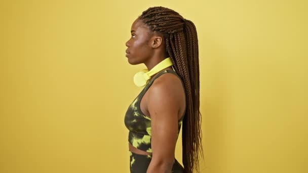 Sebevědomá africká americká žena ve sportovním oblečení pózuje s přirozeným úsměvem, vedlejší profil zastřelen přes žluté izolované pozadí - Záběry, video