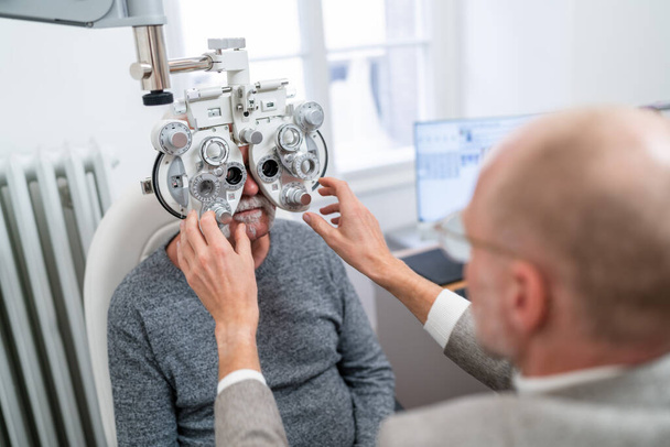 Optometr dopasowuje phoropter do testu wzroku starszego pacjenta w klinice okulistycznej. Zdjęcie z bliska. Koncepcja opieki zdrowotnej i medycyny - Zdjęcie, obraz