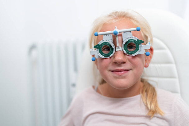 Próba keretes szemüveget viselő fiatal lány szemészeti vizsgálat során - Fotó, kép