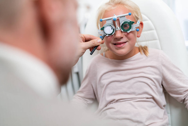 Látásvizsgálaton vagy szemészeti vizsgálaton átesett fiatal lány orvos, szemész vagy szemész általi látásvizsgálat céljából orvosi segítséggel. - Fotó, kép