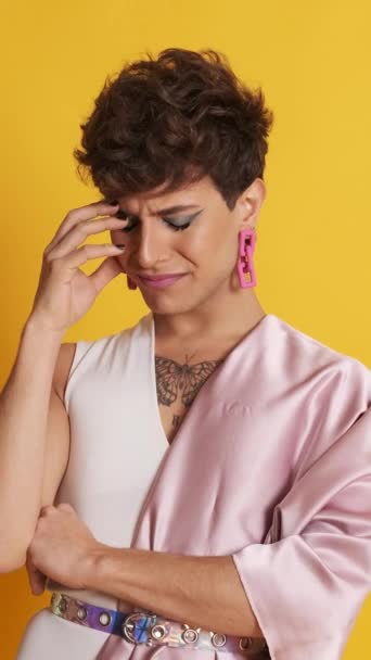 Nagranie smutnego i zaniepokojonego transseksualisty patrzącego w kamerę stojącą w studiu fotograficznym z żółtym tłem - Materiał filmowy, wideo