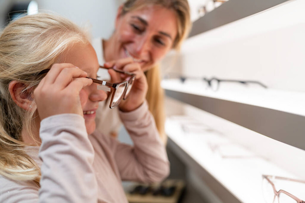 Erwachsene helfen einem Kind beim Anprobieren einer neuen Brille in einem Optikgeschäft - Foto, Bild