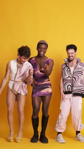 Βίντεο σε φωτογραφικό στούντιο με κίτρινο φόντο τριών χαρούμενων πολυεθνικών τρανσέξουαλ ανδρών που χορεύουν και διασκεδάζουν - Πλάνα, βίντεο