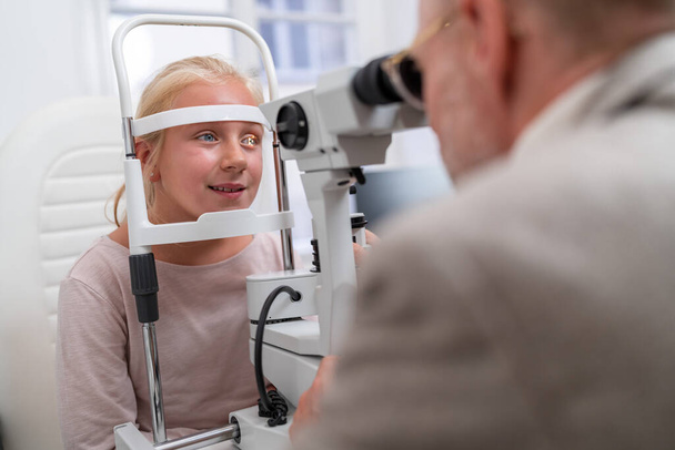 Augenuntersuchung mit jungem Mädchen beim Blick in ein Optometriegerät in Augenklinik - Foto, Bild