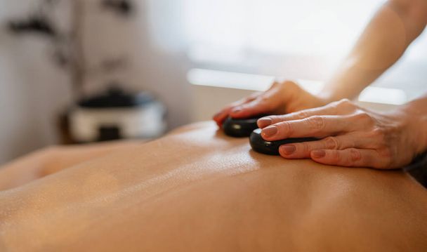 Közelkép egy forró kő masszázsról a hátán egy terapeuta kezével. beauty salon Wellness Hotel Koncepció kép - Fotó, kép