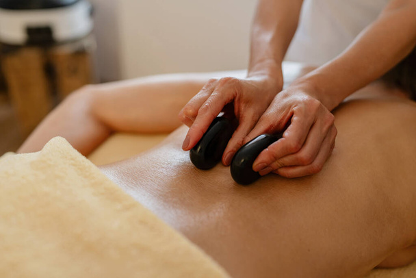 Zbliżenie gorących kamieni masażu terapii na gołe plecy z rąk terapeutów w salonie piękności lub hotelu - Zdjęcie, obraz