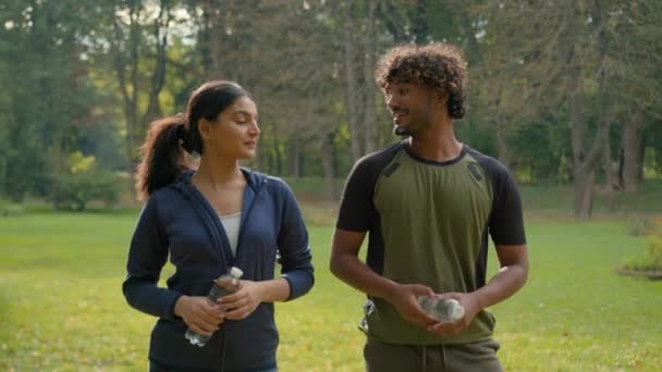 Dva sportovci běžci muži indické ženy Arabský přátelé pár muž žena v parku pozvat vítejte cvičení fitness sportovní fit trénink běží ve městě venku drží láhve přijít sem motivace - Záběry, video