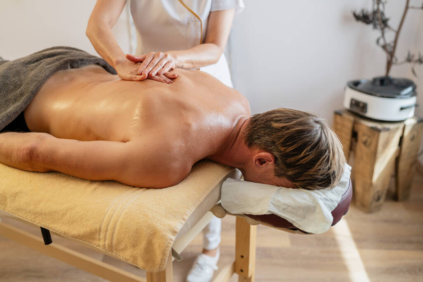 Miespuolinen asiakas saa selkähieronnan terapeutilta modernissa kylpylähotellissa - Valokuva, kuva