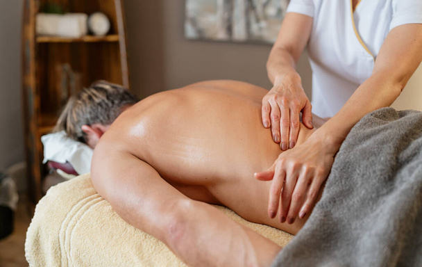 Masajista realizando masaje de espalda en cliente masculino en spa. Wellness Hotel Concept image - Foto, imagen