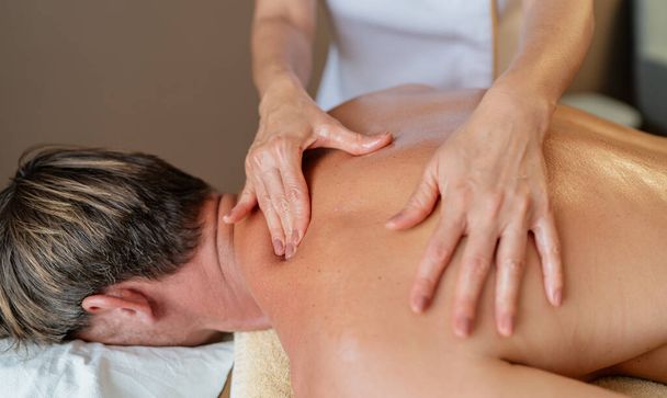Nahaufnahme eines Massagetherapeuten, der an der Schulter und am Rücken eines Klienten arbeitet - Foto, Bild