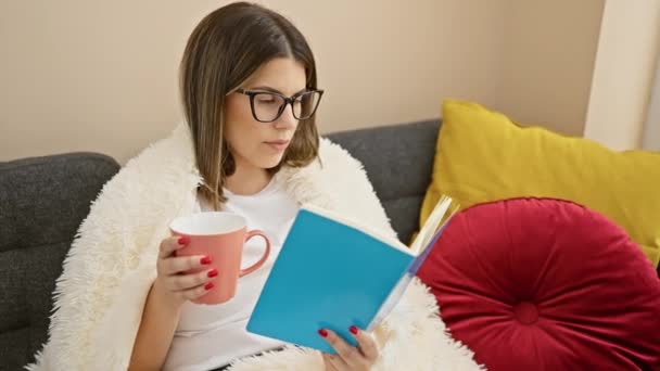 Een jonge Spaanse vrouw ontspant met een boek en mok in een gezellige woonkamer interieur. - Video