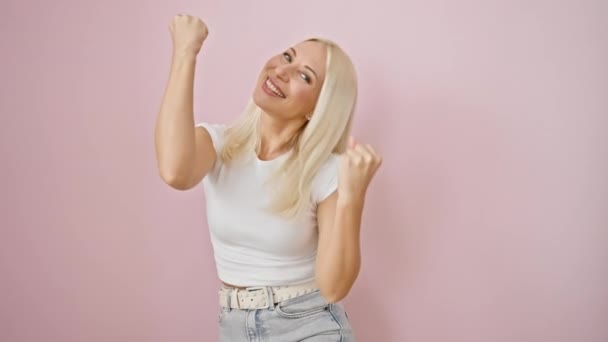 Vreugdevolle jonge blonde vrouw viert pulserende overwinning! opgewonden stand, winnaar gebaar, schreeuw van succes geïsoleerd over roze achtergrond - Video