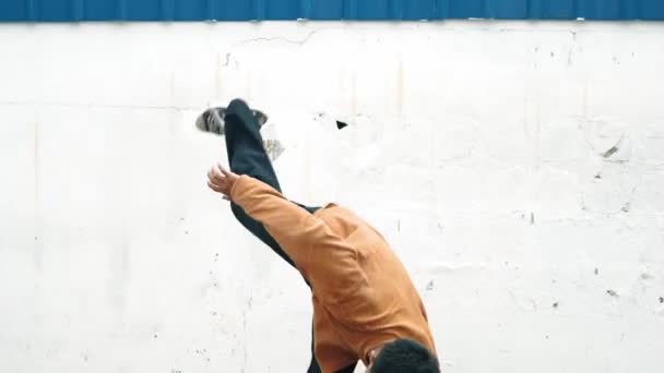 Spanyol férfi kinyújtja a karját, és break táncot jár a fal előtt. Szekrény elegáns utcai táncos alkalmi ruhát gyakorló tánc hip-hop stílusban. Kültéri sport 2024. Háttér. hiphop. - Felvétel, videó