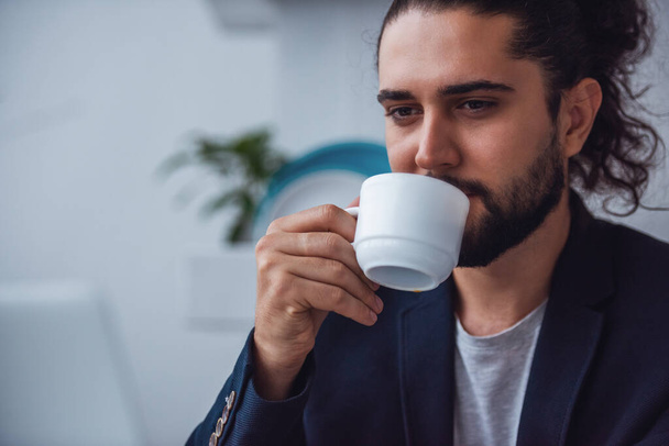 Bonito jovem empresário com longos cabelos escuros está bebendo café
 - Foto, Imagem