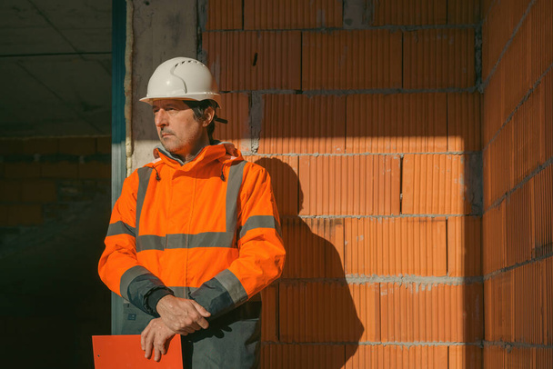 Portrait of construction engineer on building site, leaning on to unfinished wall - Foto, afbeelding