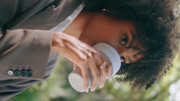 Šťastná žena pije kávu donášku v městském parku zblízka. Nádherná africká americká obchodní dáma ve stylovém obleku hledající kameru s úsměvem vertikálně video. Exotická dívka těší nápoj venku. - Záběry, video