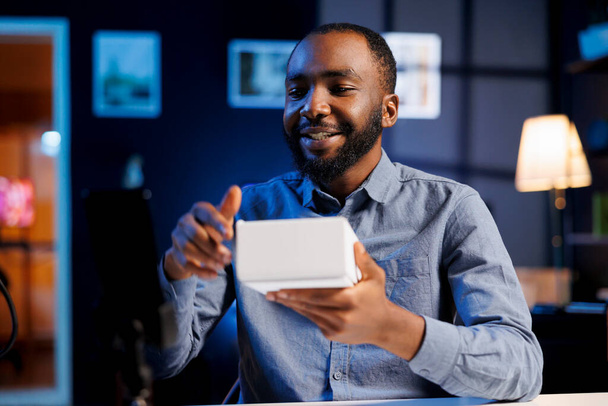 African american online show host being sponsored by partnering brand to do unboxing video on streaming platform. BIPOC man does influencer marketing, presenting viewers product advertisement - Photo, Image