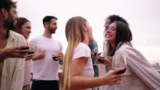 Hübsche blonde Frau blickt kokett in die Kamera und tanzt mit einer Gruppe aufgeregter multiethnischer Freunde, die sich bei einem Glas Rotwein auf einer Penthouse-Party treffen. Menschen genießen Urlaub - Filmmaterial, Video