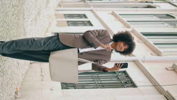 Mädchen benutzt Smartphone für Selfie im Stehen. Junge selbstbewusste afrikanisch-amerikanische Frau, die auf dem Bildschirm ein Foto im Freien macht, vertikales Video. Attraktiv entspannte Dame zu Fuß Stadt mit modernem Telefon. - Filmmaterial, Video