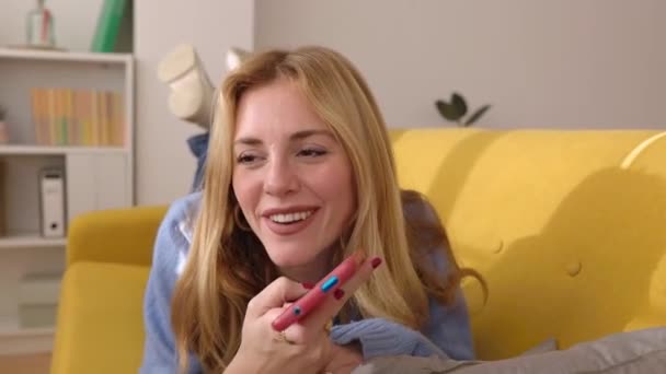 Young caucasian woman relaxing on sofa sending voice message on mobile phone app - Footage, Video