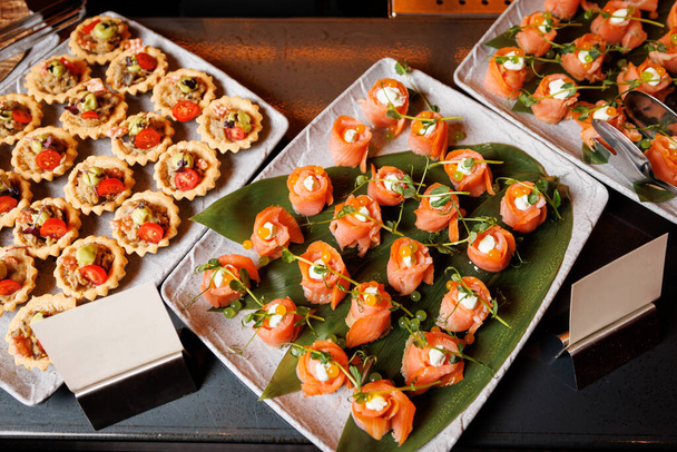 A gourmet spread of assorted appetizers, featuring succulent salmon rolls and savory tartlets, elegantly displayed on a chic catering table. - Photo, Image