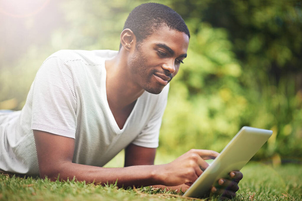 Relax, happy and tablet with black man on grass of garden for research or information in summer. Technology, internet and young person reading online ebook on green field outdoor in backyard. - Foto, Imagen