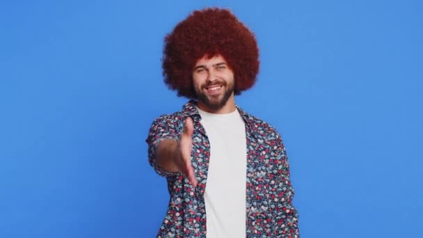 Friendly Caucasian man outstretching hand to camera offering handshake, greeting with kind smile invitation welcoming showing solidarity, trust concept. Young guy isolated on blue background indoors - Footage, Video