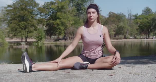 Atraktivní, flexibilní žena roztahující se v klidném prostředí parku u vody, podporující zdraví a wellness. - Záběry, video