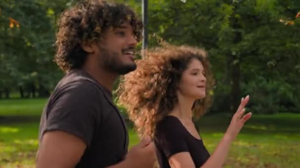 Multiracial amour couple coureurs séance d'entraînement course à pied dans la ville parc heureux gen z petite amie sport gens courir ensemble sain Caucase femme Indien homme pointant sur le chemin direction jogging à l'extérieur - Séquence, vidéo