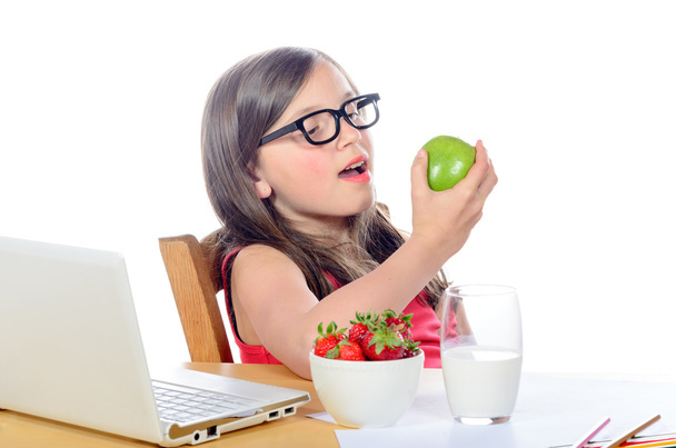 uma menina sentada em sua mesa comendo uma maçã
 - Foto, Imagem