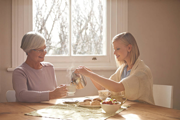Happy, grandmother and woman with tea in home for brunch, bonding or visit in retirement. Senior, grandma and girl on coffee break with food, conversation and pouring liquid with steam in morning. - Photo, Image