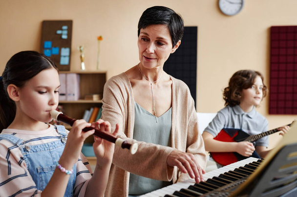 Mature teacher playing musical instruments together with student during musical lesson - Photo, Image
