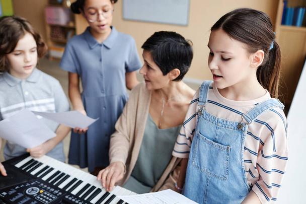 Choir of children singing songs in music class while teacher playing piano and singing together with them - Fotografie, Obrázek