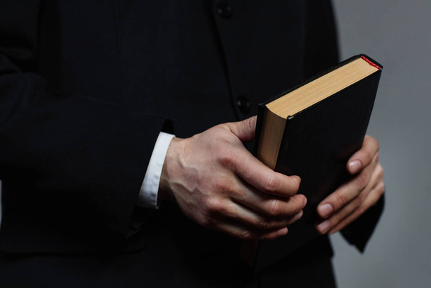 Detailní záběr pastora v černém obleku držícího biblickou knihu během kázání v kostele - Fotografie, Obrázek