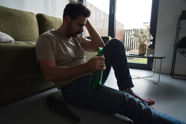 Μεθυσμένος που κάθεται στο πάτωμα ανάμεσα σε άδεια μπουκάλια. - Φωτογραφία, εικόνα