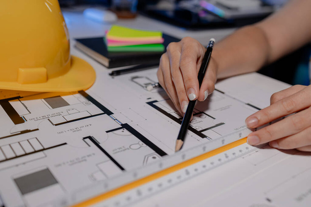 Ein Ingenieur arbeitet in einem privaten Büro mit Dokumenten, die auf dem Tisch verteilt sind. Ein Architekt analysiert sorgfältig Entwürfe mit verschiedenen Werkzeugen, um die besten Ergebnisse zu erzielen, bevor er sie an den Kunden schickt.. - Foto, Bild