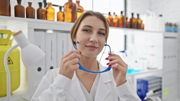 Una giovane donna indossa occhiali di sicurezza in un ambiente di laboratorio con bottiglie chimiche sullo sfondo. - Filmati, video