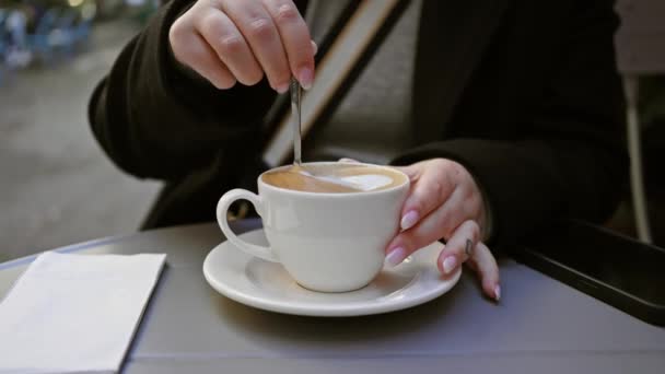 Nainen nauttii cappuccinosta katukahvilassa älypuhelimella, jossa on urbaania elämäntapaa ja virvokkeita. - Materiaali, video